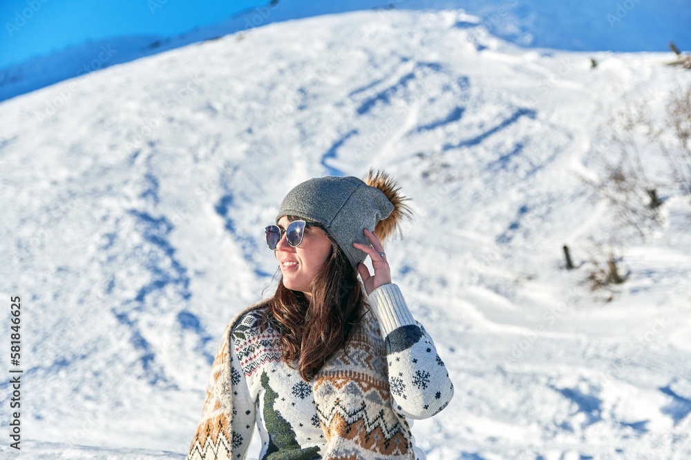 Female tourist with sunglasses and a scarf admiring the beautiful view on a snowy mountain