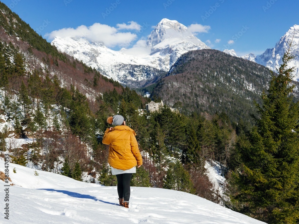 Female in a yellow coat looking at the snowy peaks and evergreen trees of the winter park