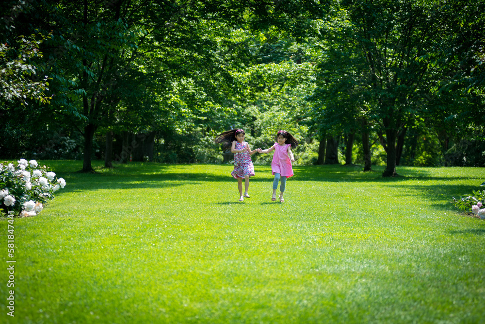 Fototapeta premium Two young asian girls running down middle of garden while holding hands