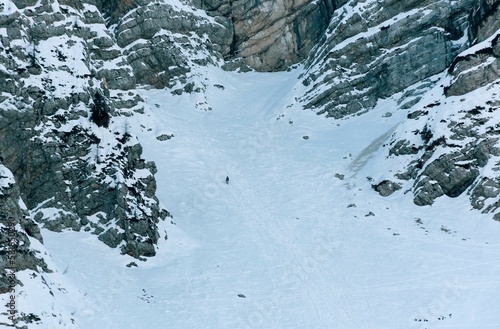 Tiny human on steep snowy slope on a rocky mountain