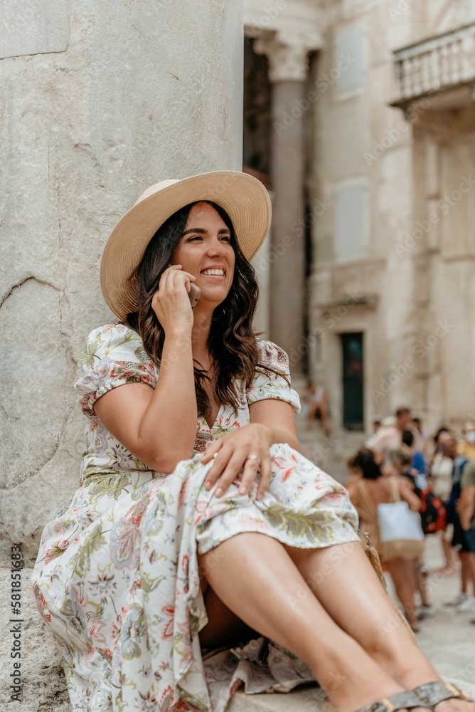Girl in a hat talking on a cell phone while sitting by a column of ancient building in Split Croatia