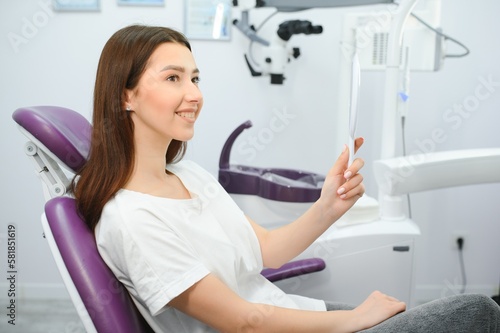 Woman looking in the mirror and smiling after checkup at dentist office.