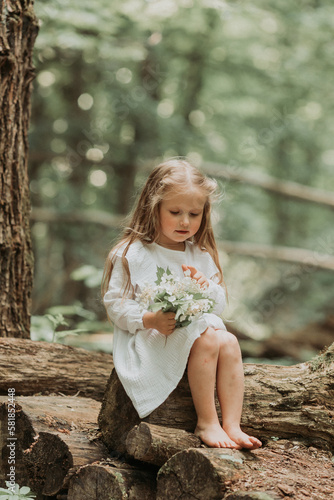 a cute little girl with long hair in a white cotton dress runs barefoot in the woods in summer. The concept of Earth Day. Save the planet