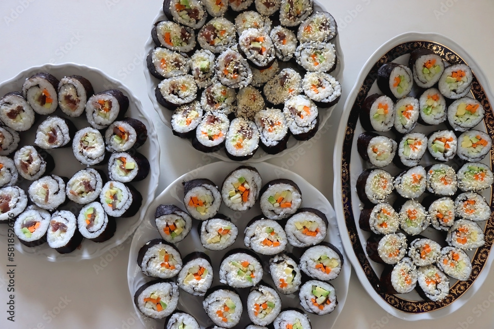 Plates with homemade sushi rolls on white table. Tuna and vegetable sushi, and vegetarian cream cheese and vegetable sushi. Top view. Plates with homemade sushi rolls on white table. Tuna and vegetable sushi, and vegetarian cream cheese and vegetable sushi. Top view.