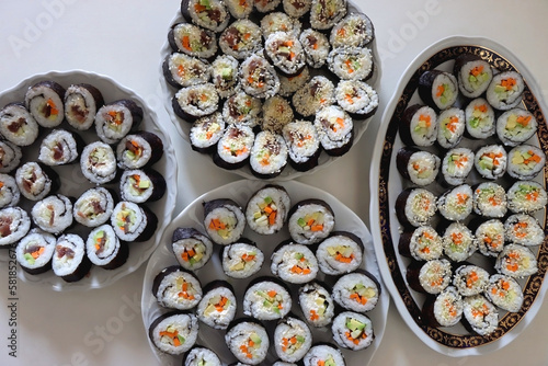 Plates with homemade sushi rolls on white table. Tuna and vegetable sushi, and vegetarian cream cheese and vegetable sushi. Top view.