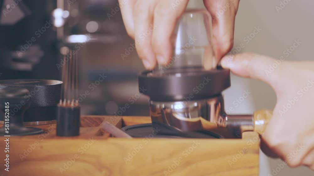 Close up 4K of barista's hands preparing (grinding and tampering) coffee powder at wooden counter in coffee shop in the morning shows concept of food and beverage business for professional career. Close up 4K of barista's hands preparing (grinding and tampering) coffee powder at wooden counter in coffee shop in the morning shows concept of food and beverage business for professional career.