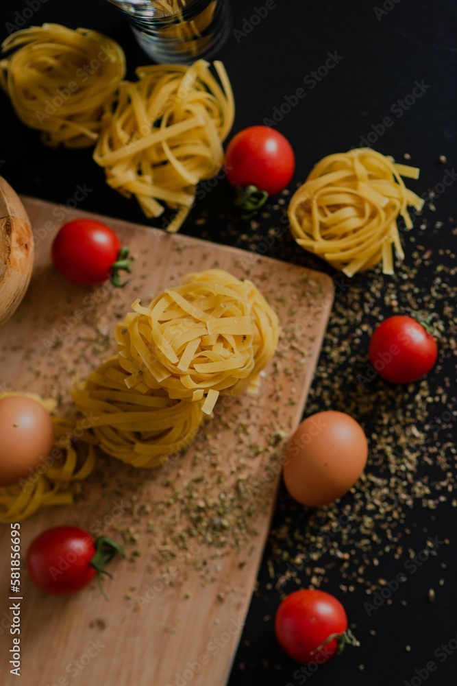 Wooden board with pasta, two eggs and cherry tomatoes with spices scattered over it Wooden board with pasta, two eggs and cherry tomatoes with spices scattered over it