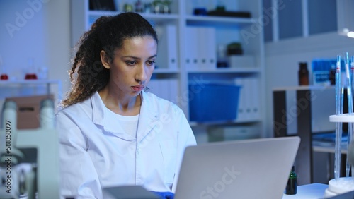 Concentrated woman lab worker tracking chemical reaction online on laptop