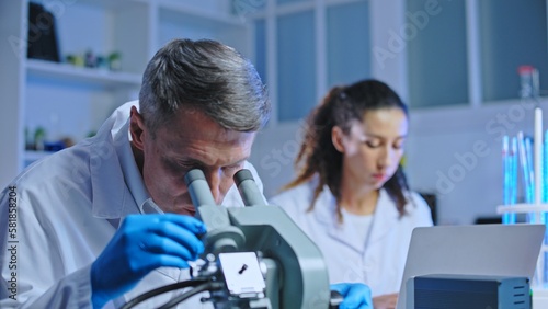 Oncology doctor examining tissue sample under microscope, clinical diagnostic lab