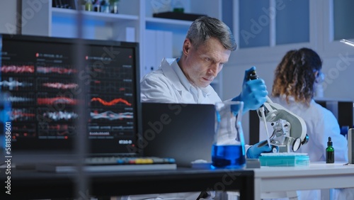 Attentive scientist studying liquid sample under microscope, microbiology lab