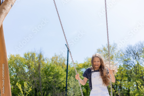 a happy little girl rides on a swing on a playground in summer on a sunny day. Children's Day
