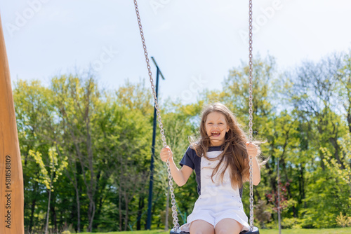 a happy little girl rides on a swing on a playground in summer on a sunny day. Children's Day