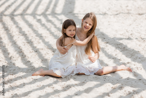 two happy little girls with long hair in summer dresses play on a sandy beach in summer