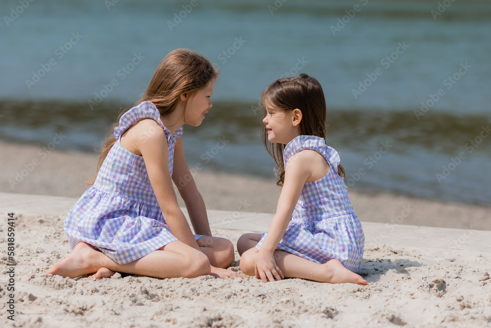 happy little girls with long hair play on a sandy beach near the sea on a sunny day. Children's Day.Space for text happy little girls with long hair play on a sandy beach near the sea on a sunny day. Children's Day.Space for text