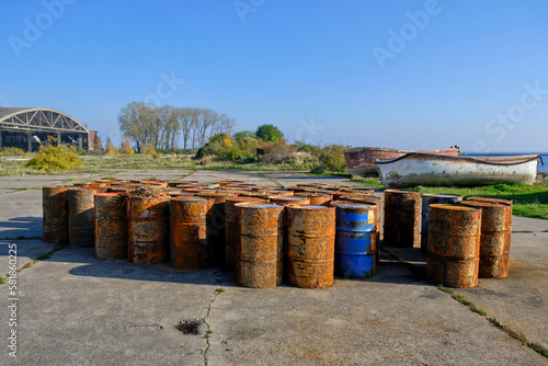 Rusty fuel barrels shore against background old hangar and boats.