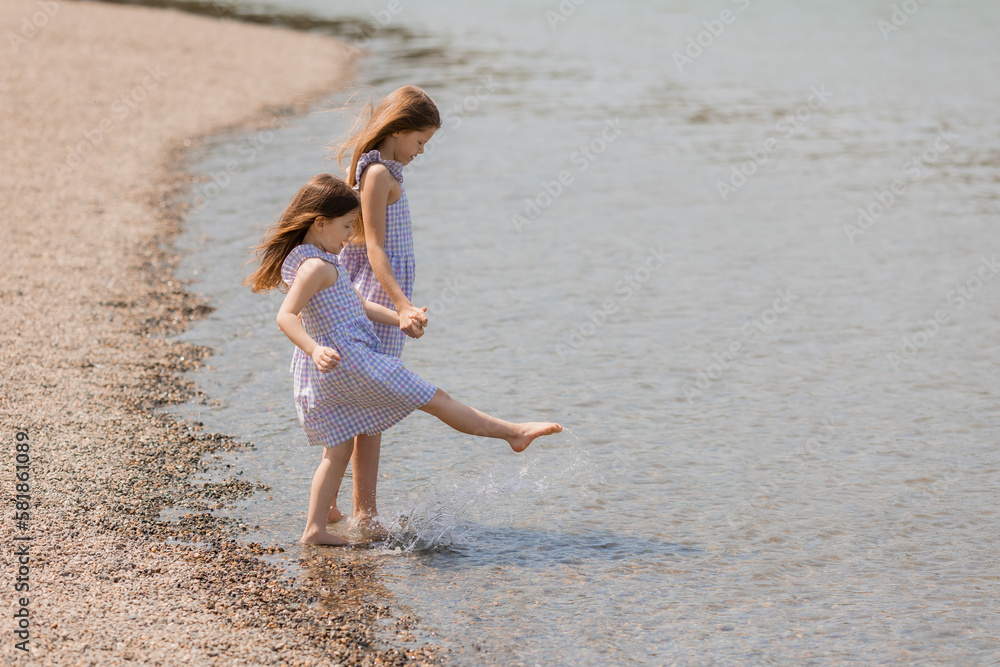 Naklejka premium two happy little girls are walking near the lake in summer. Earth Day. Children's Day.Space for text