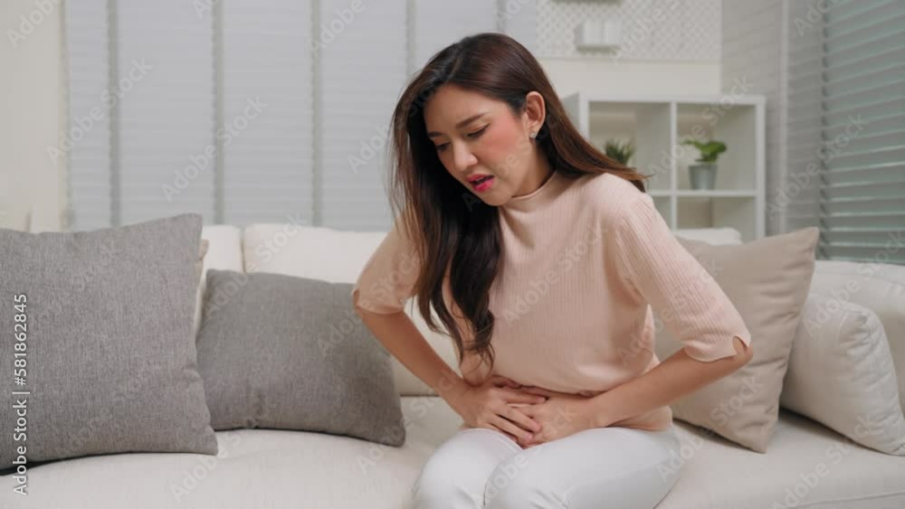 Young Asian woman having menstrual pain and sitting on couch in living room at home Young Asian woman having menstrual pain and sitting on couch in living room at home