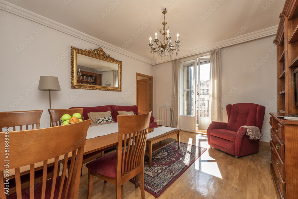 Fototapeta premium Living room furnished with a dining table with matching chairs and a sofa upholstered in dark red fabric, a matching wing chair and access to the terrace with aluminum and glass doors
