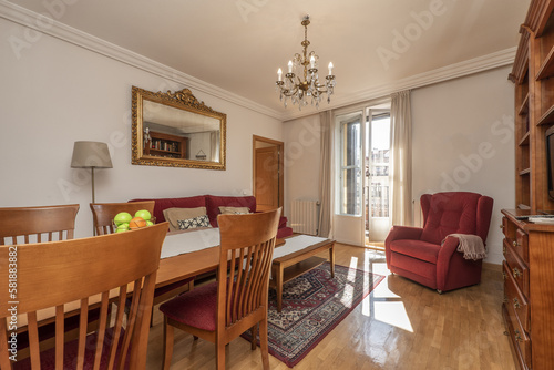 Living room furnished with a dining table with matching chairs and a sofa upholstered in dark red fabric, a matching wing chair and access to the terrace with aluminum and glass doors