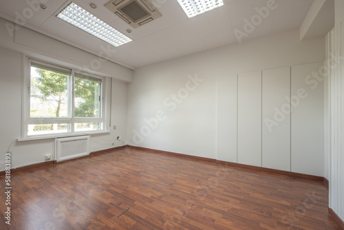 Empty office of an office with reddish laminated floors, technical ceilings and double aluminum windows
