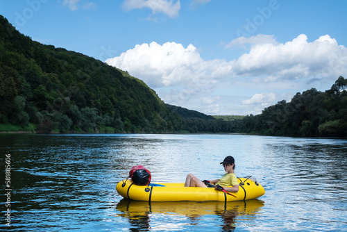 Young boy on yellow packraft boat with red padle on a sunrise river. Packrafting background. Active lifestile concept