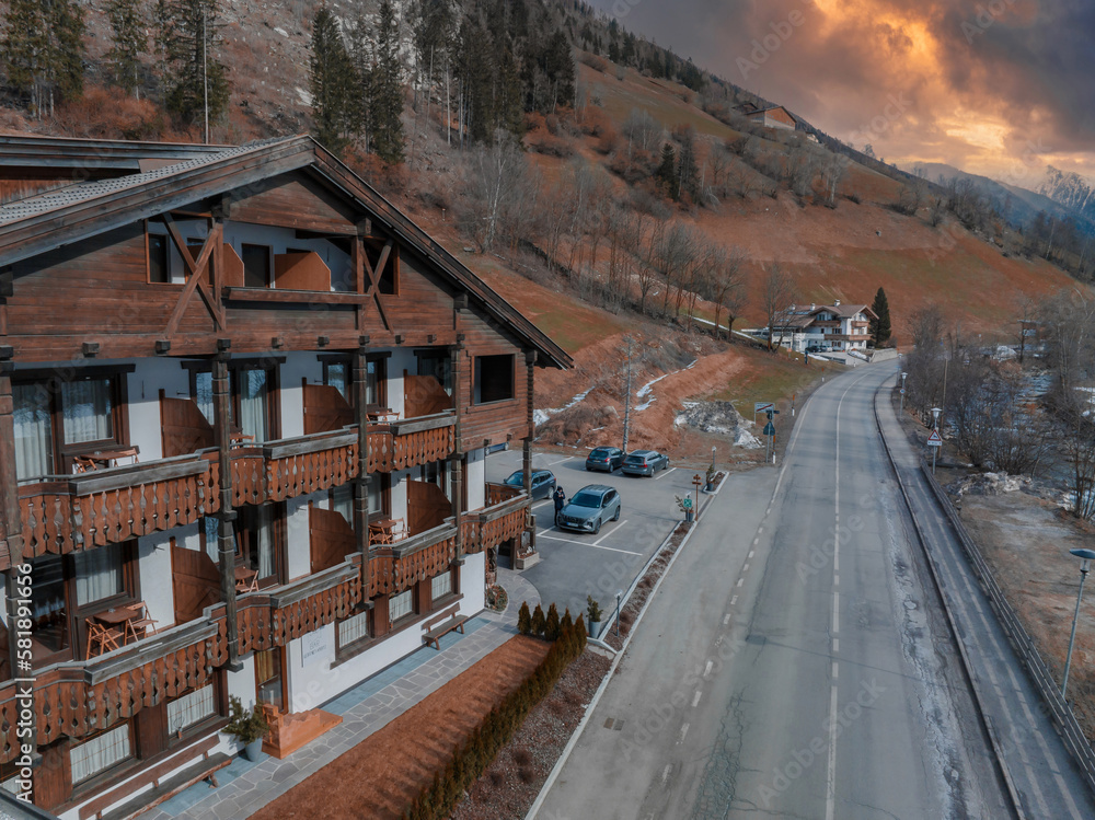 Fototapeta premium Typical wooden alpine house decorated with flowers in the middle of the village on a cloudy winter day, Tyrol, Italy. Aerial view.