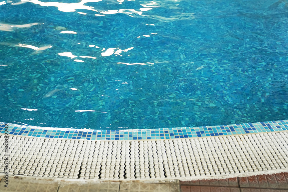 A step at the entrance to the fiberglass pool with clean, refreshing blue water in the spa area of the resort. White wooden flooring made of teak or larch board. High quality photo