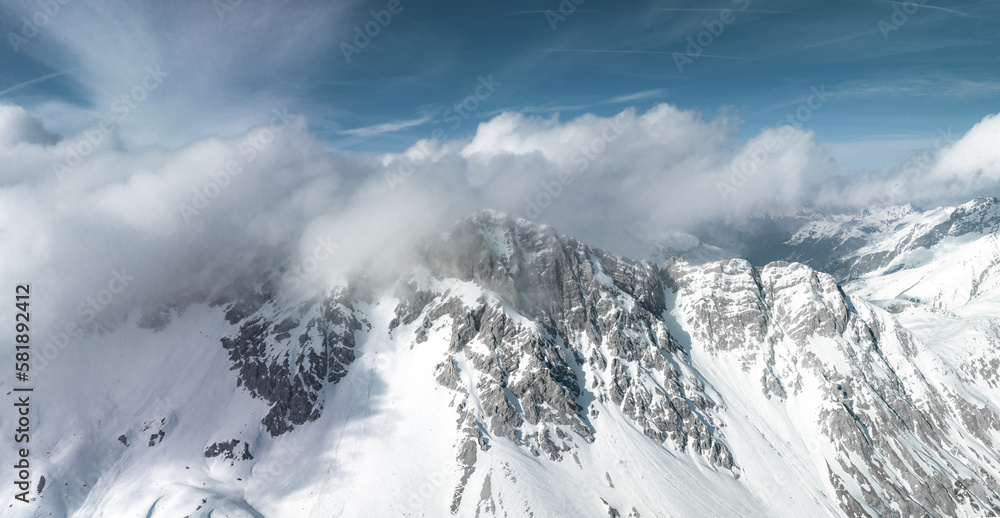 Alpine landscape with peaks covered by snow and clouds. Magical clouds covering peaks of the mountains at the famous St. Anton am Arlberg ski resort.