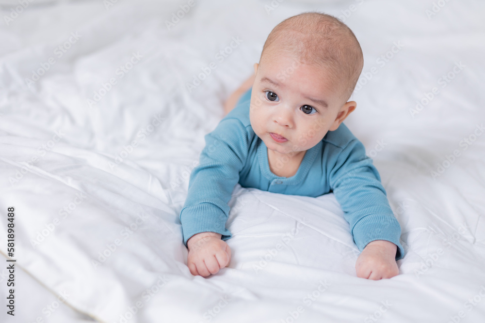 portrait of a cute baby in a blue bodysuit lying on his stomach to the bed. The child is 4 months old. Space for text portrait of a cute baby in a blue bodysuit lying on his stomach to the bed. The child is 4 months old. Space for text