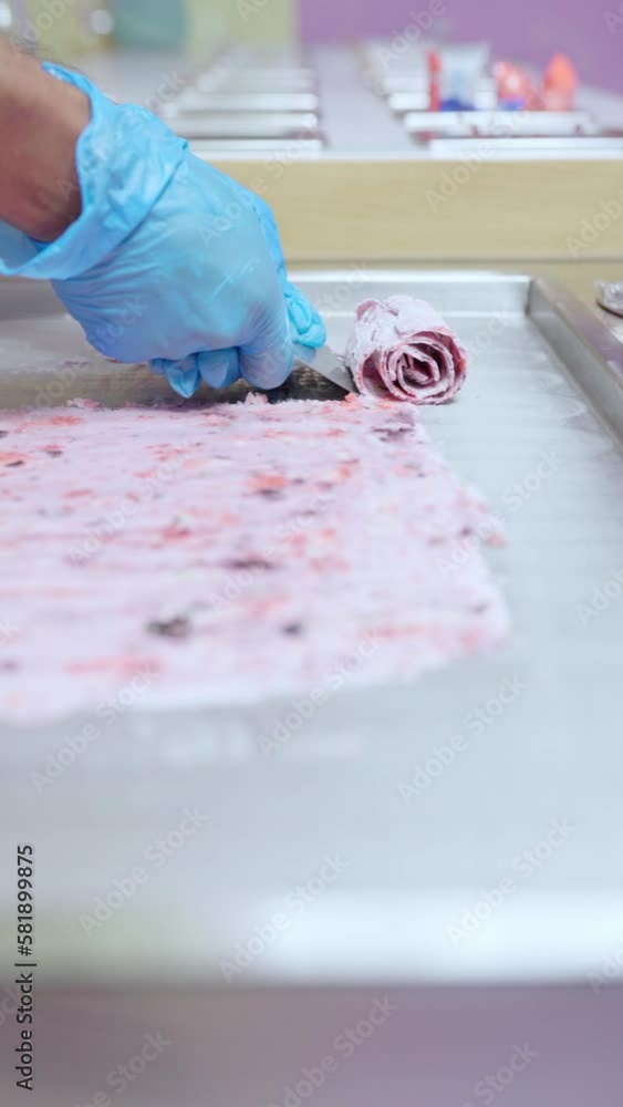 A worker is using a spatula to roll a rolled fruits of the forest on a freeze machine A worker is using a spatula to roll a rolled fruits of the forest on a freeze machine
