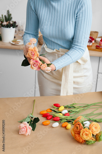 Female florist making bouquet of beautiful spring flowers at light wooden table