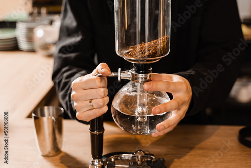 Barista is holding siphon before starting boiling water inside syphon. Process of brewing siphon coffee in cafe.