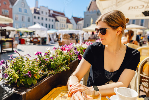 Smiling woman with sunglasses sits in shady cafe seat in colourful sunny European town square