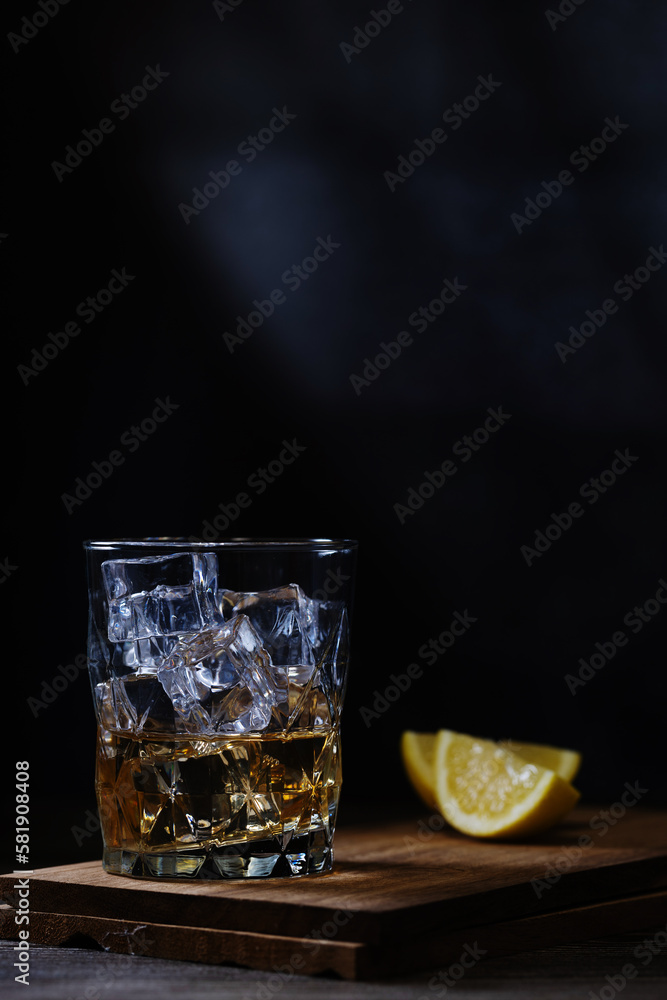 whiskey with ice and lemon on a wooden stand and black background whiskey with ice and lemon on a wooden stand and black background
