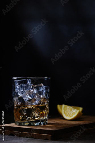 whiskey with ice and lemon on a wooden stand and black background