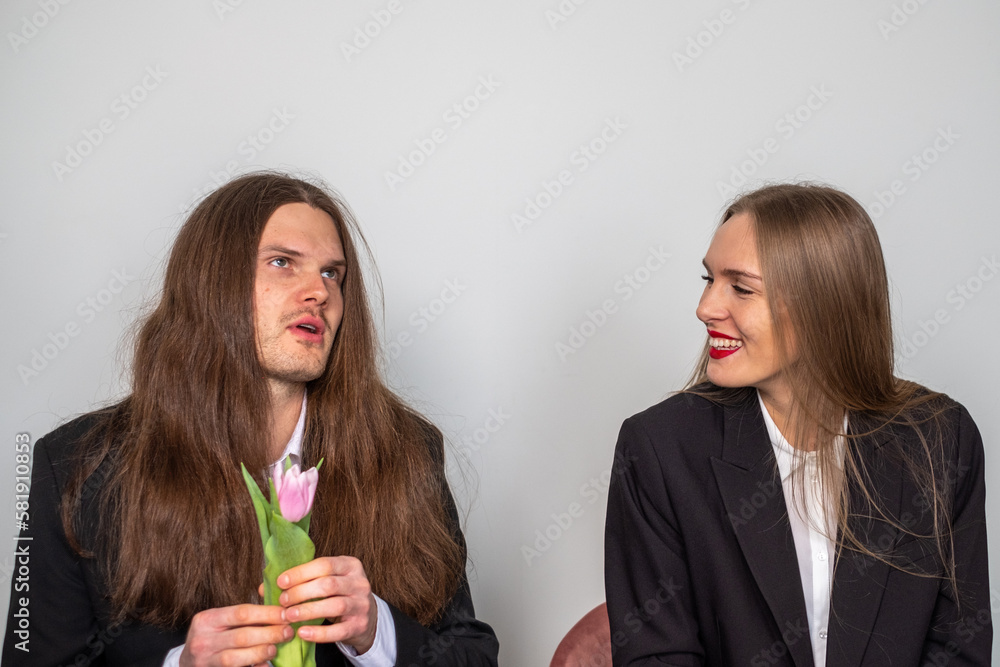 Couple in suits. Man with long, brown hair holding a tulip, looking at something. Woman smiling and laughing. Couple in suits. Man with long, brown hair holding a tulip, looking at something. Woman smiling and laughing.