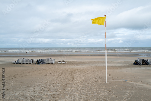 A windy day at the beach in The Netherlands, with a yellow flag and an expansive horizon of sea, sky, clouds and land.