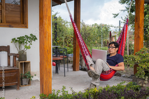 Man with glasses sitting in a hammock working with his computer in a garden