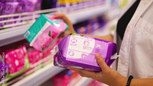 Woman choosing menstrual pads on shelf with feminine hygiene products.