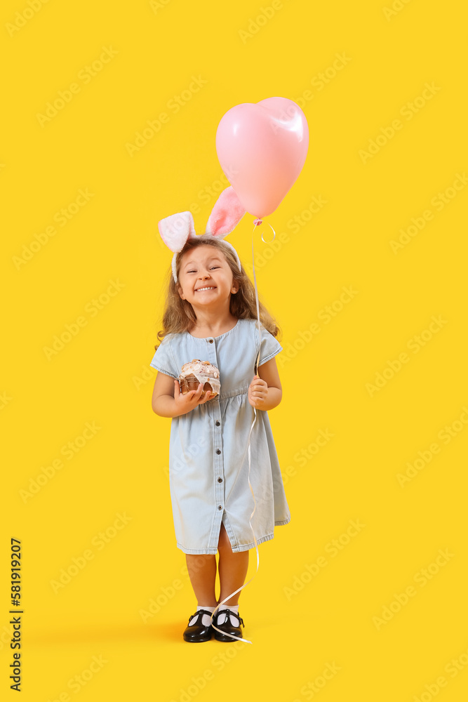Little girl in bunny ears with Easter cake and balloon on yellow background Little girl in bunny ears with Easter cake and balloon on yellow background