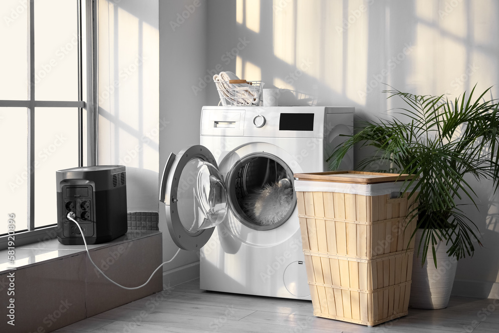 Washing machine plugged in portable power station in laundry room Stock