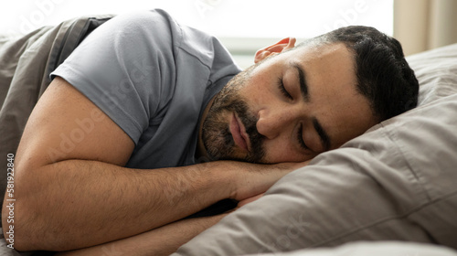 European man sleeping on side, lying with eyes closed, resting peacefully in his comfortable bed at home, closeup shot