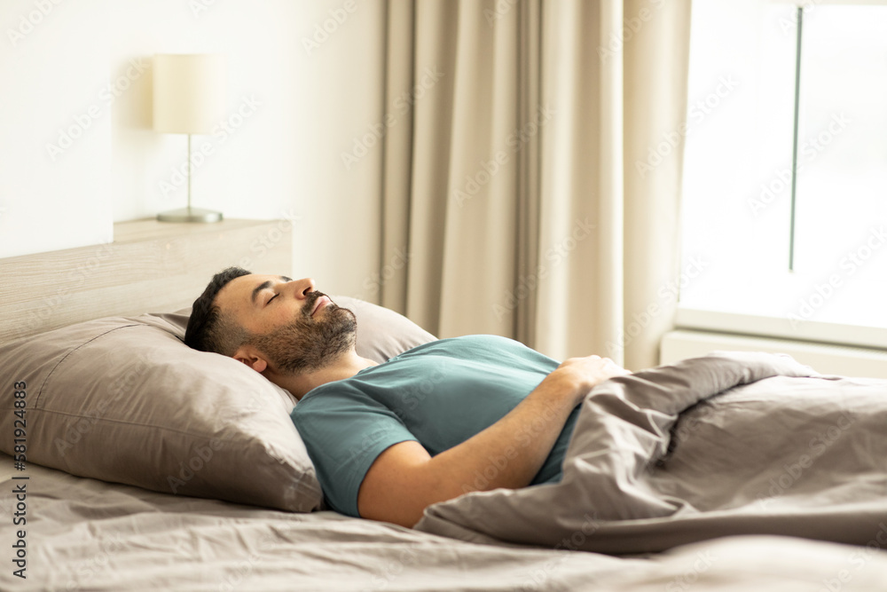 Calm man sleeping lying on back covered with blanket, resting, napping in bed in light bedroom interior, free copy space Calm man sleeping lying on back covered with blanket, resting, napping in bed in light bedroom interior, free copy space
