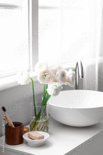 Vase with ranunculus flowers and sink on table in bathroom