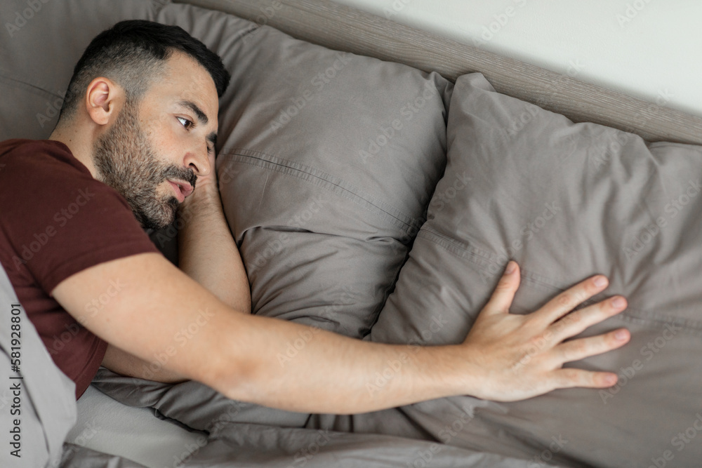 Sad middle aged man touching pillow, suffering from loneliness after breakup, lying in bed at home, above view, free space. Lonely male having depression Sad middle aged man touching pillow, suffering from loneliness after breakup, lying in bed at home, above view, free space. Lonely male having depression