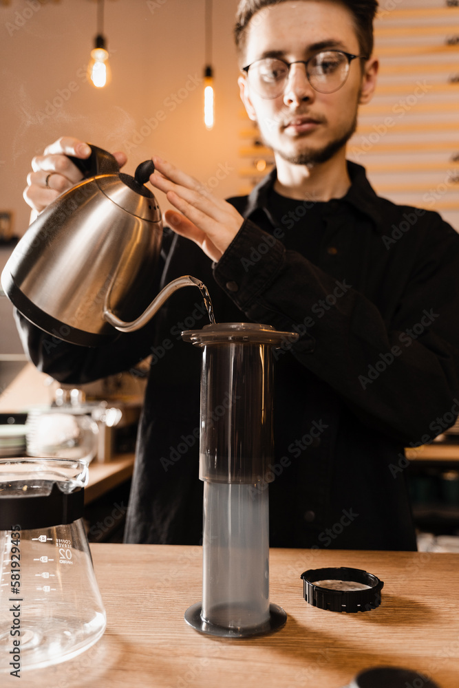 Barista is pouring hot water from drip kettle to aeropress. Process of brewing aeropress. Pouring hot water over roasted and ground coffee beans in aeropress.