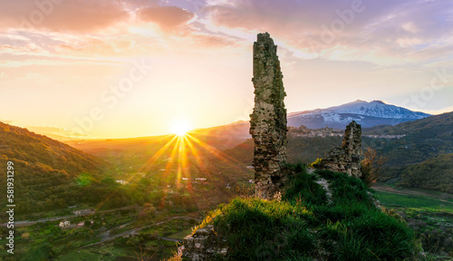 beautiful sunset or sunrise landscape of ancient ruins on a top of a hill with green mountains with white snow top on background © Yaroslav
