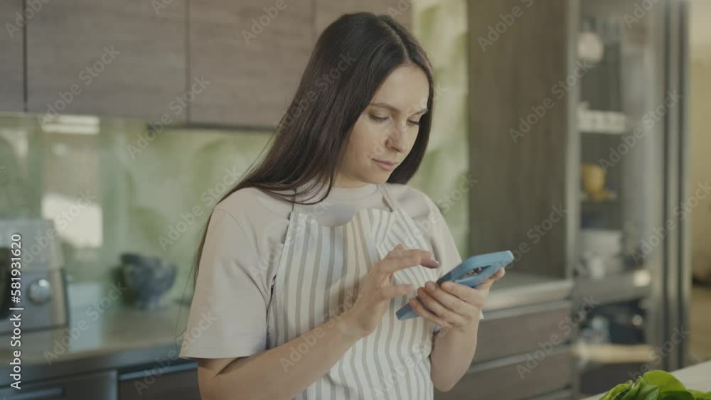 Young beautiful girl ilooking for recipe for dish on her phone. Girl smiles. Slow motion Young beautiful girl ilooking for recipe for dish on her phone. Girl smiles. Slow motion