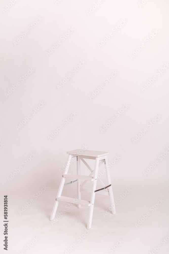 Wooden white ladder - stool. A room in a photo studio. White wall and floor. Copy space. Place for text and design. Wooden white ladder - stool. A room in a photo studio. White wall and floor. Copy space. Place for text and design.