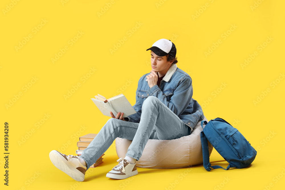 Male student reading book on yellow background Male student reading book on yellow background